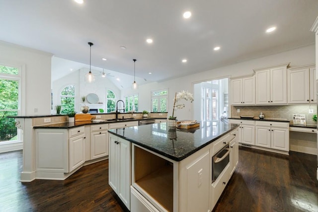 kitchen featuring dark wood-type flooring, a sink, vaulted ceiling, backsplash, and a center island