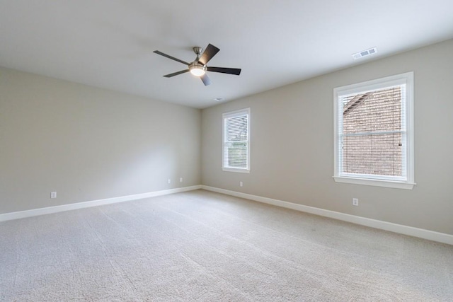 empty room with light carpet, a ceiling fan, visible vents, and baseboards