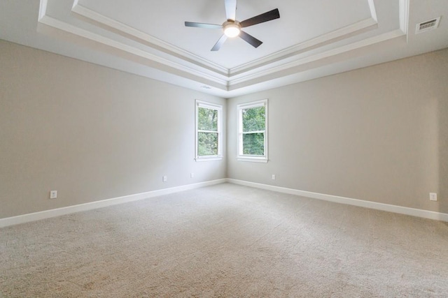 carpeted empty room featuring visible vents, baseboards, ceiling fan, a tray ceiling, and crown molding