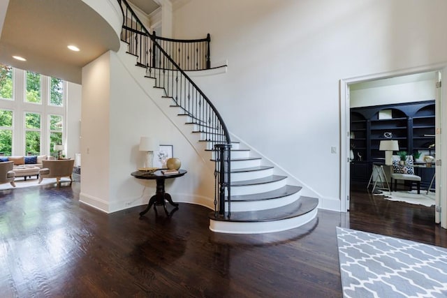 stairs featuring a towering ceiling, baseboards, wood finished floors, and recessed lighting