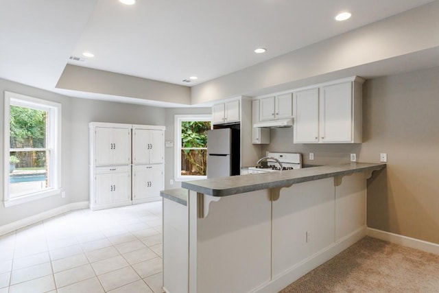 kitchen featuring visible vents, freestanding refrigerator, a kitchen breakfast bar, a peninsula, and baseboards