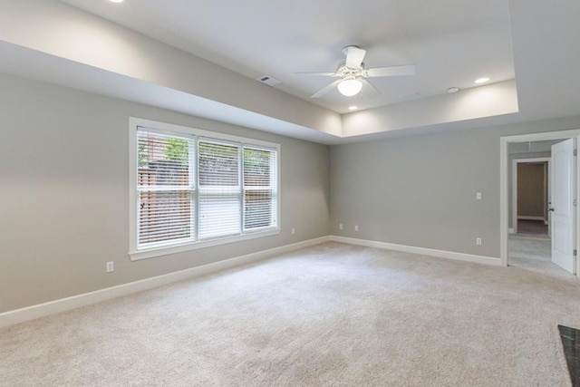 spare room with recessed lighting, a raised ceiling, light carpet, and baseboards