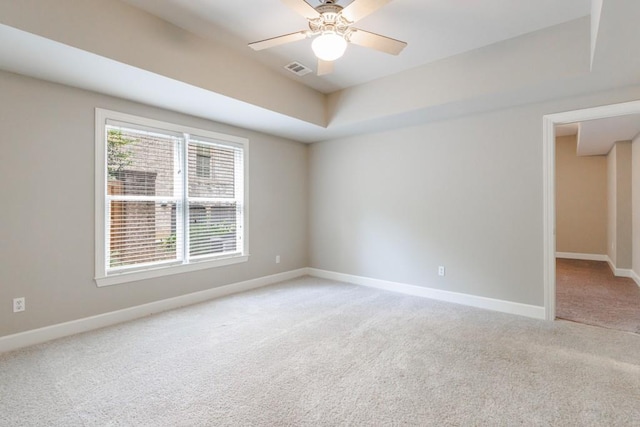 spare room featuring light carpet, a ceiling fan, visible vents, baseboards, and a raised ceiling