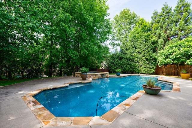 view of swimming pool featuring a pool with connected hot tub, fence, and a patio