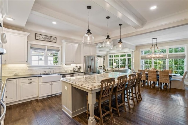 kitchen with a kitchen island, a breakfast bar, decorative light fixtures, dark stone countertops, and stainless steel fridge