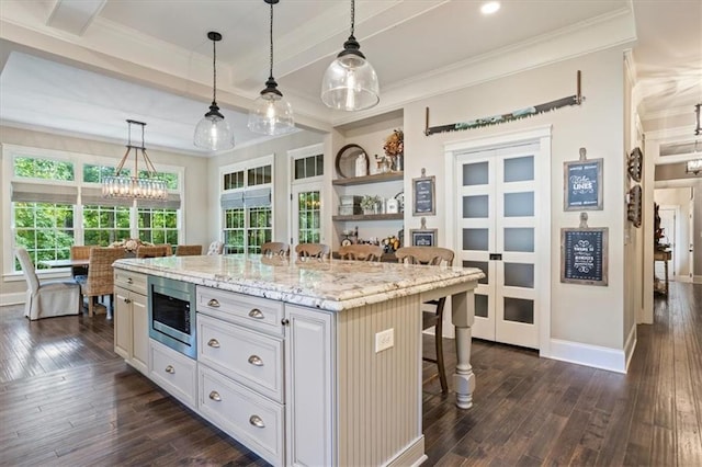 kitchen featuring stainless steel microwave, decorative light fixtures, a breakfast bar area, and a kitchen island