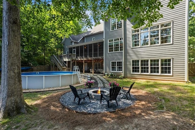 rear view of house with a pool side deck, a fire pit, and a sunroom