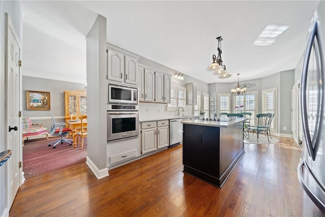 kitchen with appliances with stainless steel finishes, an inviting chandelier, hanging light fixtures, a kitchen island, and decorative backsplash