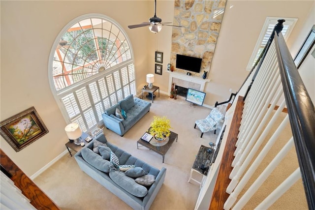 carpeted living room with a high ceiling, a stone fireplace, a wealth of natural light, and ceiling fan