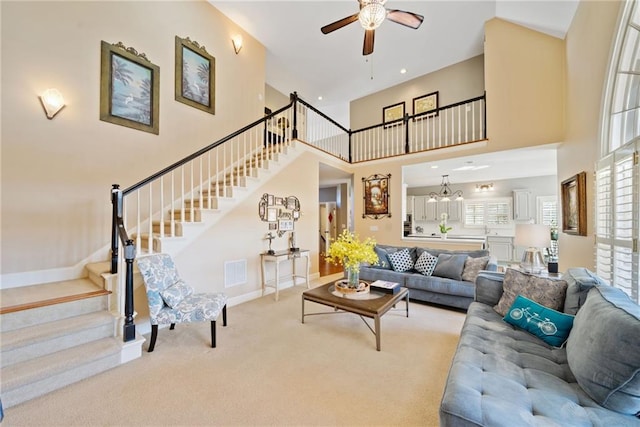 carpeted living room featuring ceiling fan with notable chandelier and a high ceiling