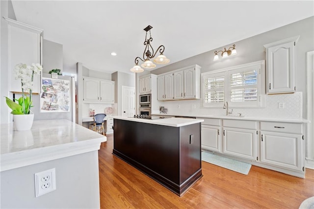 kitchen featuring sink, appliances with stainless steel finishes, light hardwood / wood-style floors, a kitchen island, and decorative light fixtures