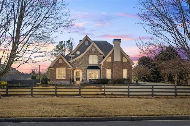 view of front facade with a fenced front yard, stone siding, a chimney, and a front lawn