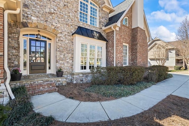 view of exterior entry with a standing seam roof, roof with shingles, metal roof, and brick siding