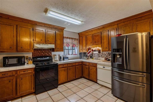 kitchen with tile counters, black appliances, light tile patterned floors, and a textured ceiling