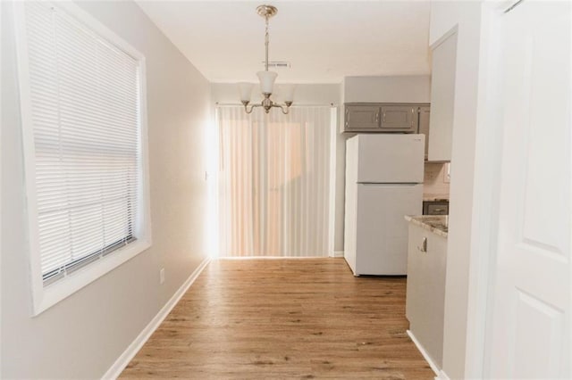 unfurnished dining area with light wood-type flooring and an inviting chandelier