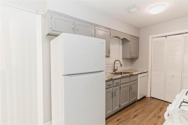 kitchen featuring gray cabinetry, white appliances, sink, light wood-type flooring, and light stone counters