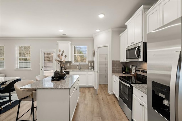 kitchen featuring a kitchen island, a breakfast bar, white cabinetry, light stone countertops, and appliances with stainless steel finishes