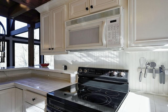 kitchen featuring black / electric stove, white microwave, tile patterned flooring, and tile counters