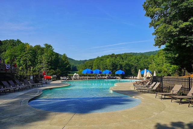 community pool featuring fence, a wooded view, and a patio