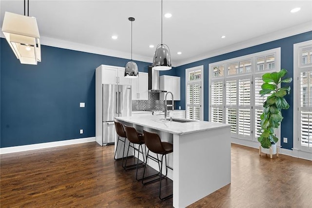 kitchen with high end fridge, sink, hanging light fixtures, an island with sink, and white cabinets