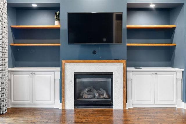 unfurnished living room featuring a premium fireplace, dark wood-type flooring, and built in shelves