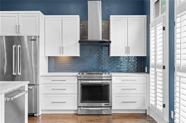 kitchen featuring white cabinetry, appliances with stainless steel finishes, light stone counters, and wall chimney range hood