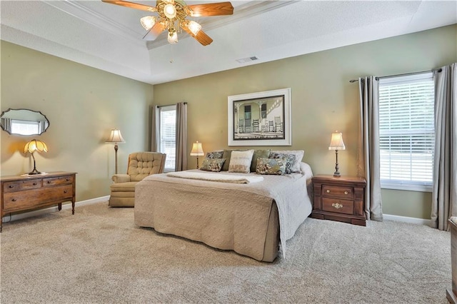 bedroom with light carpet, a tray ceiling, multiple windows, and ceiling fan