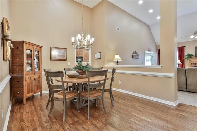 dining space with hardwood / wood-style flooring, ceiling fan with notable chandelier, and high vaulted ceiling