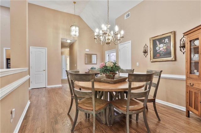 dining space with an inviting chandelier, wood-type flooring, and high vaulted ceiling