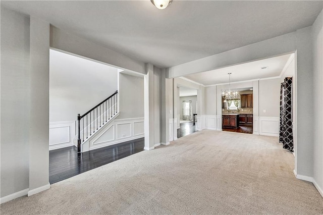 unfurnished living room featuring an inviting chandelier, dark carpet, and ornamental molding