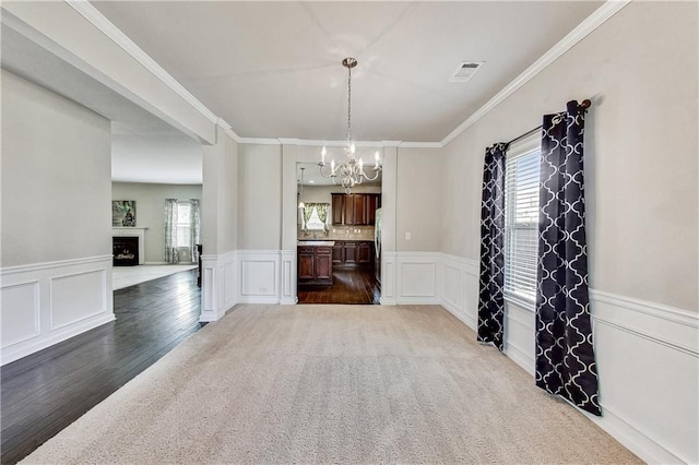 unfurnished dining area with ornamental molding, carpet flooring, and a notable chandelier