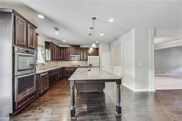 kitchen featuring an island with sink, sink, hanging light fixtures, light stone counters, and stainless steel appliances