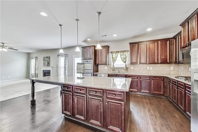 kitchen featuring pendant lighting, stainless steel appliances, dark hardwood / wood-style floors, a center island, and light stone countertops