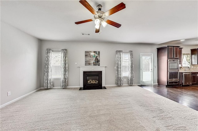 unfurnished living room with dark colored carpet, a wealth of natural light, and ceiling fan