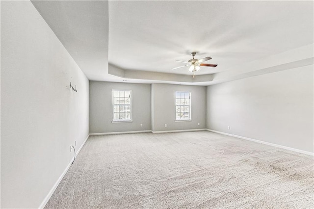 carpeted empty room with a raised ceiling and ceiling fan