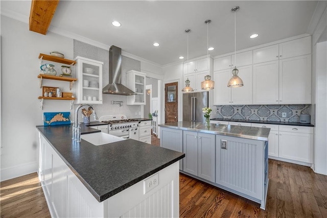kitchen with ornamental molding, dark countertops, wall chimney range hood, high quality fridge, and a sink