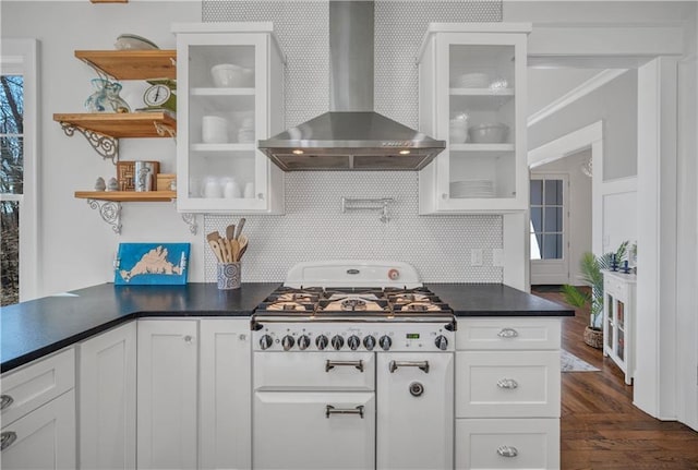 kitchen featuring wall chimney range hood, dark wood-style flooring, dark countertops, tasteful backsplash, and white cabinets