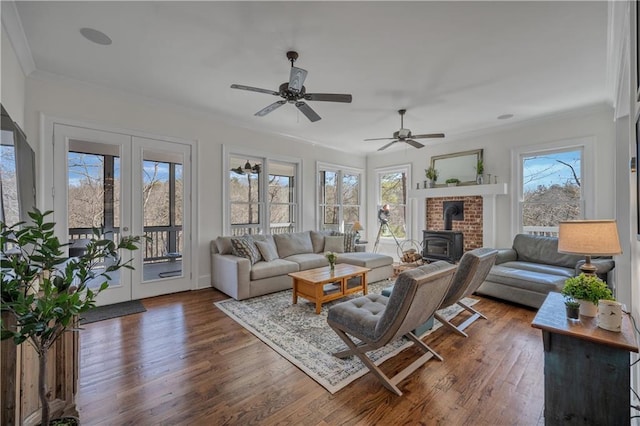 living area with french doors, a ceiling fan, dark wood-style flooring, a wood stove, and ornamental molding