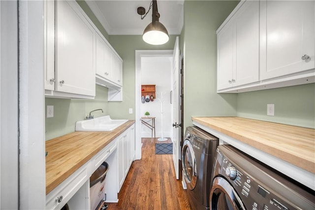 laundry room featuring washing machine and clothes dryer, dark wood finished floors, cabinet space, a sink, and ornamental molding