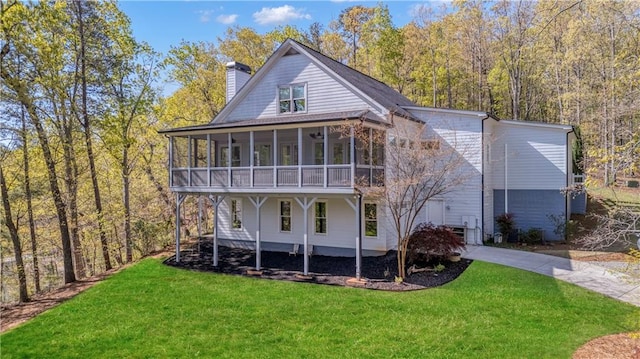 rear view of property featuring concrete driveway, a lawn, a chimney, and a sunroom