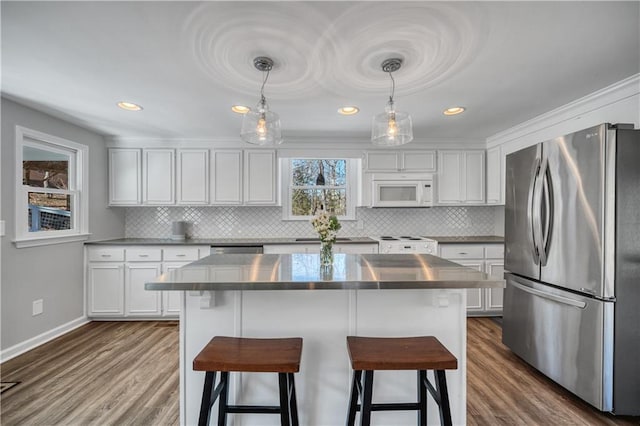 kitchen with freestanding refrigerator, a kitchen bar, white cabinetry, and white microwave