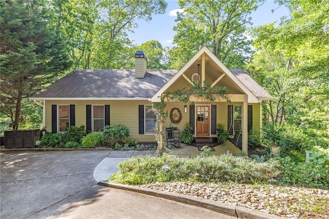 view of front of home with a chimney, covered porch, and roof with shingles