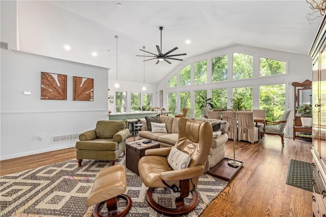 living room with wood finished floors, wainscoting, a ceiling fan, and vaulted ceiling