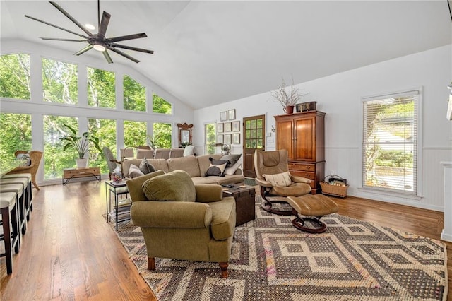 living room with ceiling fan, wainscoting, wood finished floors, and high vaulted ceiling