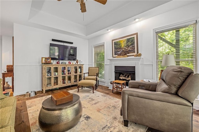 living area with a ceiling fan, a fireplace, plenty of natural light, wood finished floors, and wainscoting