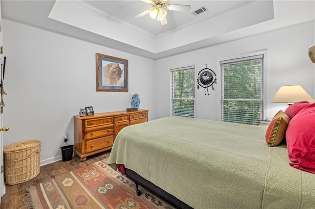bedroom featuring a raised ceiling, wood finished floors, ornamental molding, ceiling fan, and baseboards