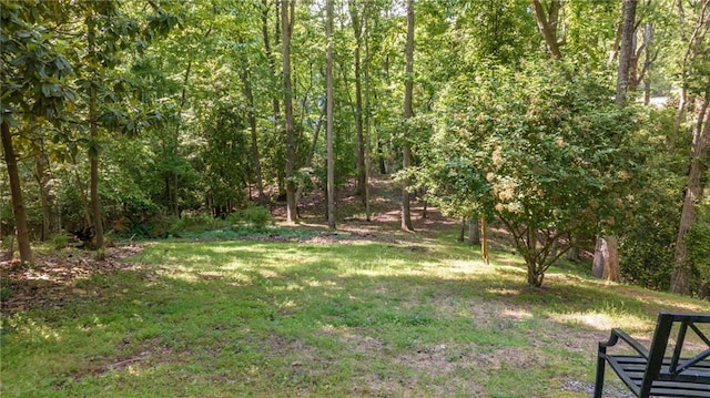 view of green lawn featuring a forest view