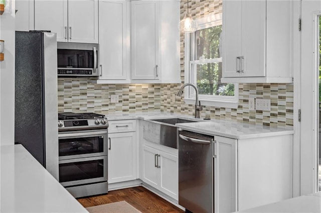 kitchen with stainless steel appliances, a sink, white cabinets, backsplash, and hanging light fixtures