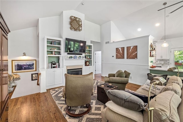 living room featuring wood finished floors, a glass covered fireplace, high vaulted ceiling, and recessed lighting