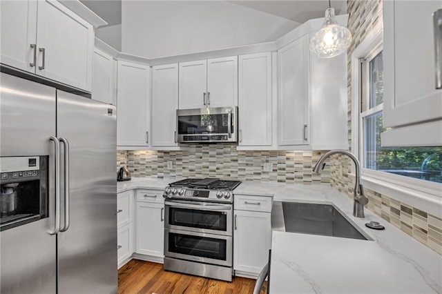 kitchen featuring appliances with stainless steel finishes, a sink, white cabinets, and vaulted ceiling